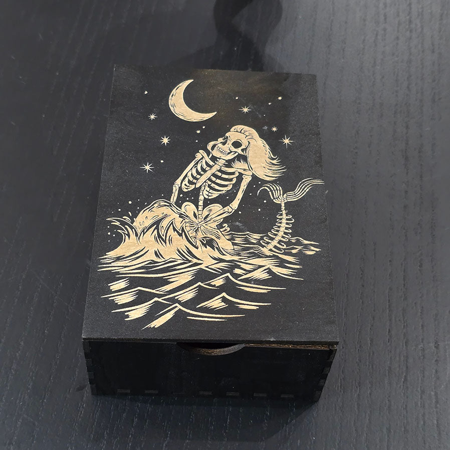 Black wooden box with a skeleton mermaid design engraved on a dark surface