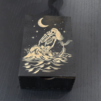 Black wooden box with a skeleton mermaid design engraved on a dark surface