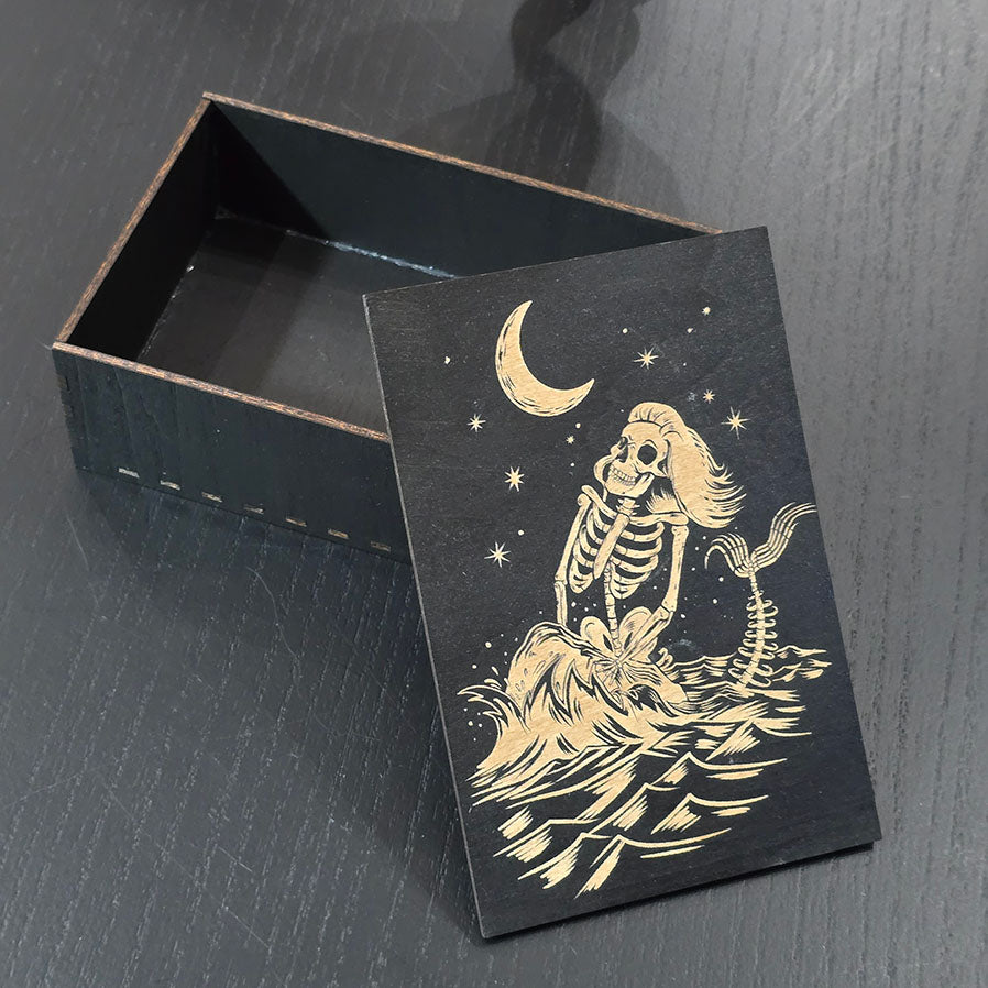 Black wooden box with a skeleton mermaid design engraved on a dark surface